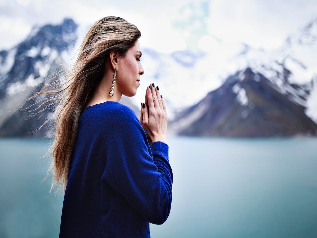 woman standing by lake, hand in prayer pose